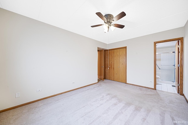 unfurnished bedroom with ceiling fan, light colored carpet, a closet, and ensuite bath