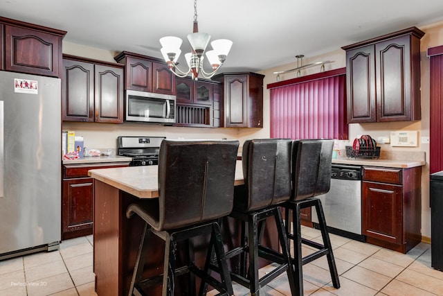 kitchen with a center island, light tile patterned floors, a kitchen breakfast bar, a notable chandelier, and stainless steel appliances