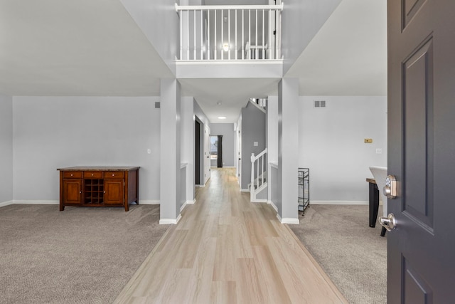 entrance foyer featuring baseboards, stairway, visible vents, and light colored carpet