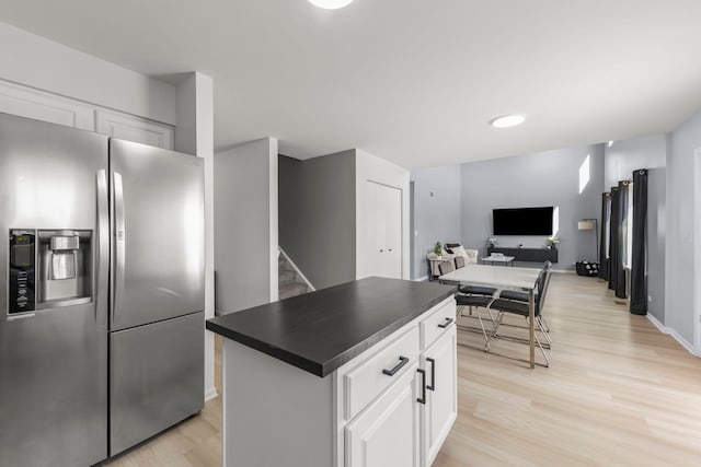 kitchen featuring light wood finished floors, dark countertops, stainless steel fridge, and white cabinets