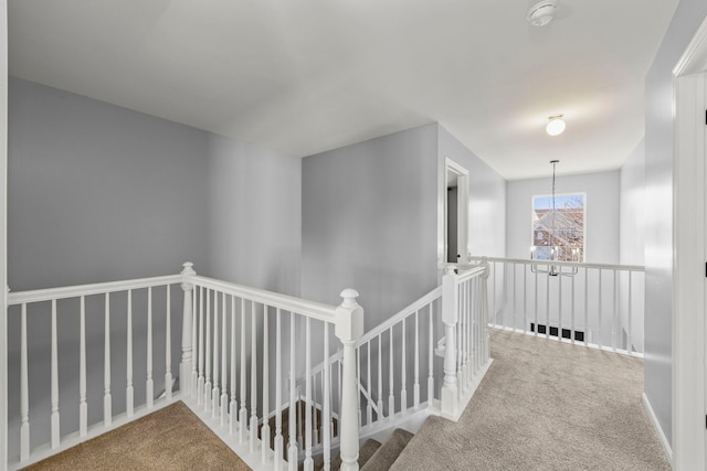 hallway with carpet flooring, an upstairs landing, and an inviting chandelier