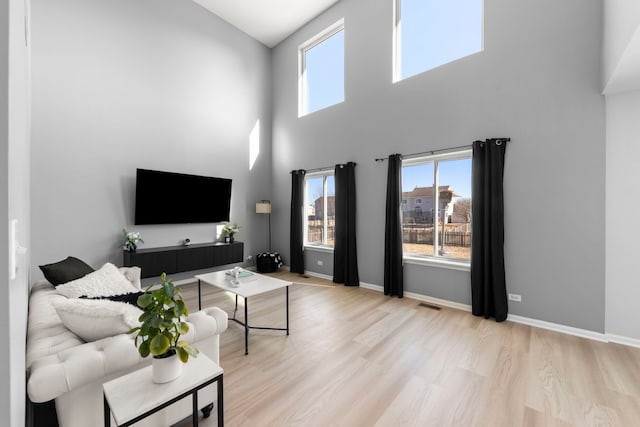 living room featuring visible vents, a towering ceiling, baseboards, and wood finished floors