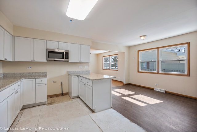 kitchen with visible vents, white cabinetry, stainless steel microwave, and baseboards