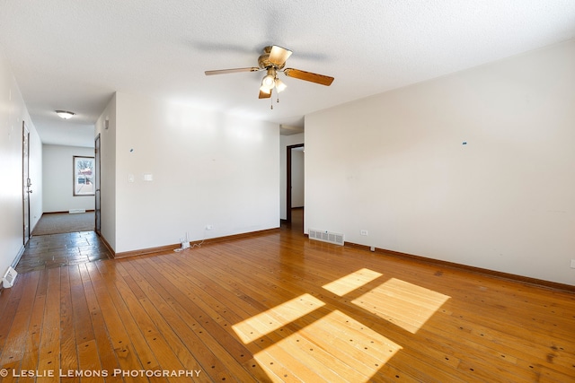 spare room featuring wood finished floors, visible vents, a ceiling fan, baseboards, and a textured ceiling