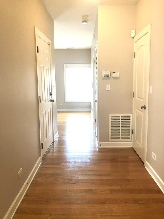 hallway with wood finished floors, visible vents, and baseboards