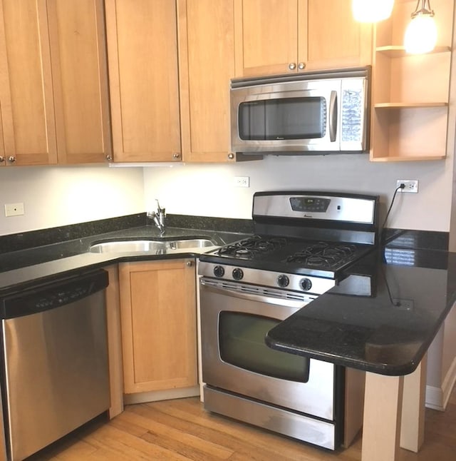 kitchen with dark stone counters, light wood finished floors, appliances with stainless steel finishes, and a sink