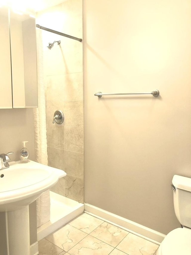 bathroom with a stall shower, toilet, baseboards, and a sink