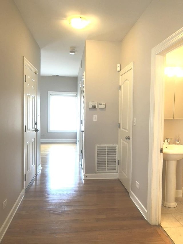 hall featuring visible vents, baseboards, and wood finished floors