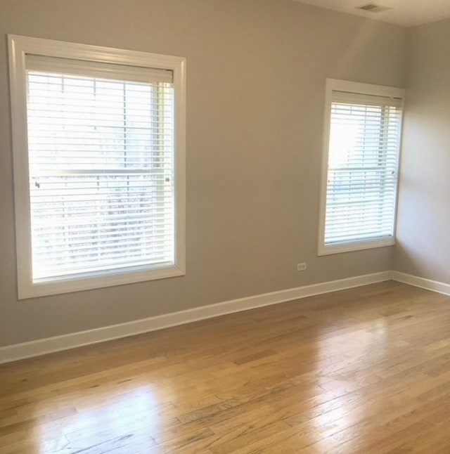 empty room featuring plenty of natural light, baseboards, and light wood-type flooring