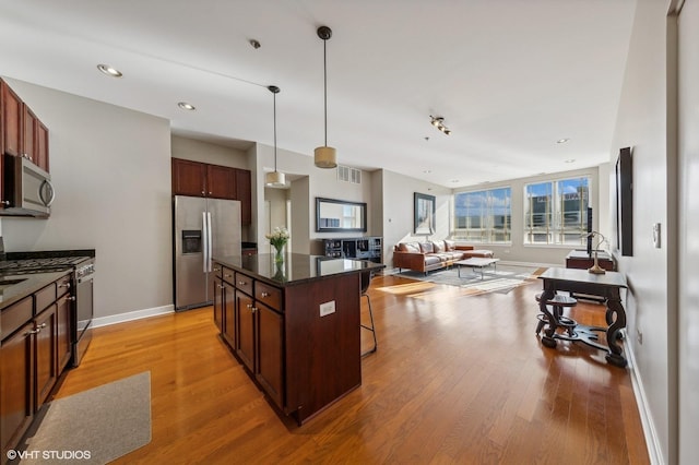 kitchen featuring appliances with stainless steel finishes, pendant lighting, a kitchen bar, a center island, and light hardwood / wood-style flooring