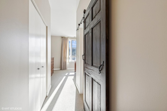 hallway with a barn door and light carpet