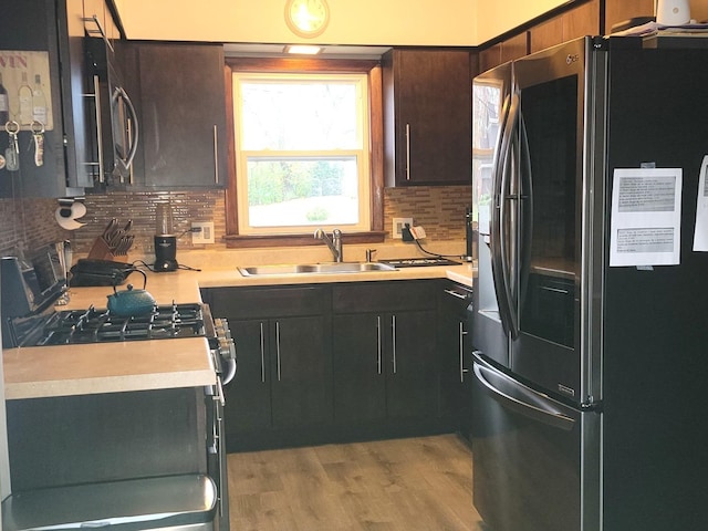 kitchen featuring sink, dark brown cabinets, light wood-type flooring, stainless steel appliances, and decorative backsplash