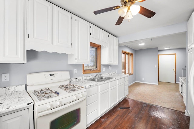 kitchen with white range with gas cooktop, baseboards, white cabinets, light countertops, and a sink