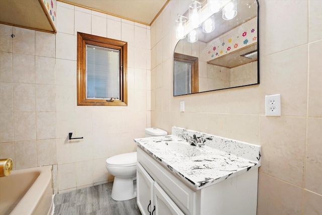 full bathroom with toilet, a tub, wood finished floors, vanity, and tile walls