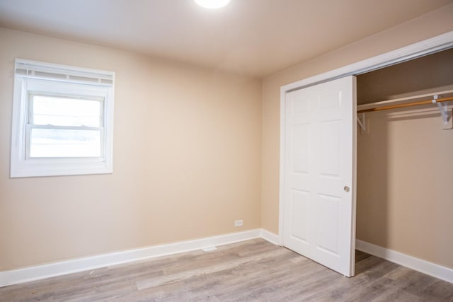 unfurnished bedroom featuring light wood finished floors, baseboards, and a closet