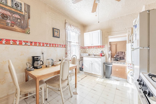 kitchen featuring light countertops, freestanding refrigerator, ceiling fan, a textured ceiling, and stainless steel gas range oven