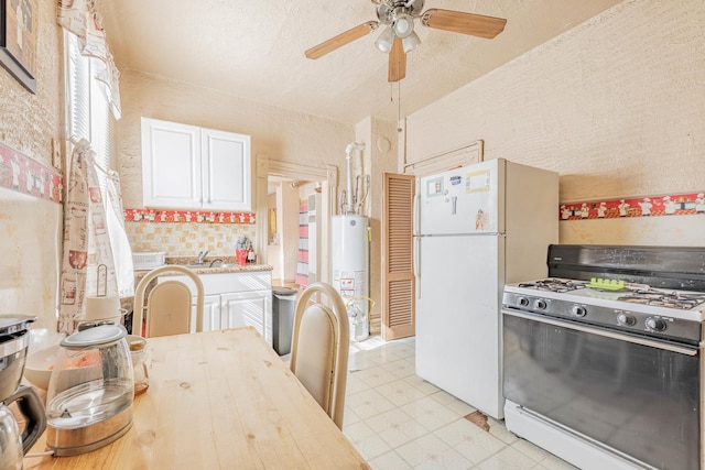 kitchen with a ceiling fan, white cabinets, water heater, freestanding refrigerator, and range with gas cooktop