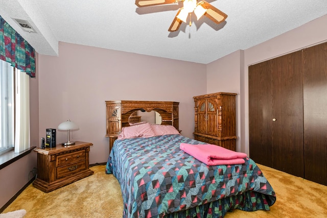 bedroom with ceiling fan, a closet, light carpet, and a textured ceiling