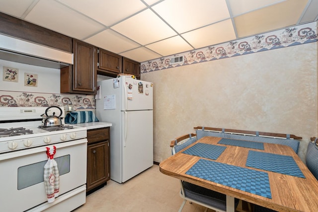 kitchen featuring premium range hood, white appliances, dark brown cabinets, and a drop ceiling