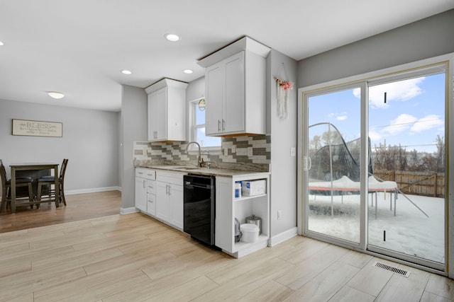 kitchen with tasteful backsplash, dishwasher, sink, white cabinets, and light hardwood / wood-style flooring