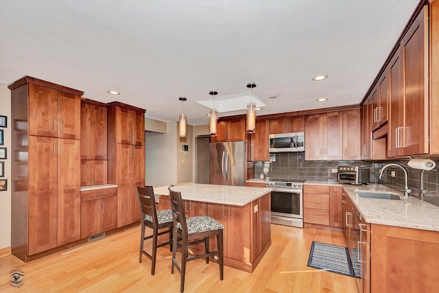 kitchen featuring a kitchen island, pendant lighting, sink, light stone counters, and stainless steel appliances