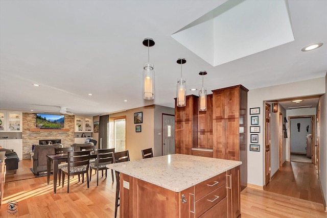 kitchen with pendant lighting, light hardwood / wood-style flooring, a center island, light stone countertops, and a large fireplace