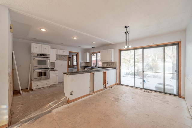 kitchen featuring double oven, backsplash, kitchen peninsula, white cabinets, and hanging light fixtures