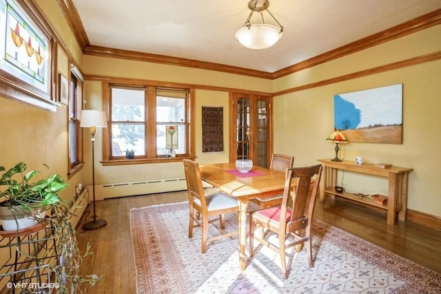 dining area with a baseboard heating unit, ornamental molding, wood finished floors, and baseboards