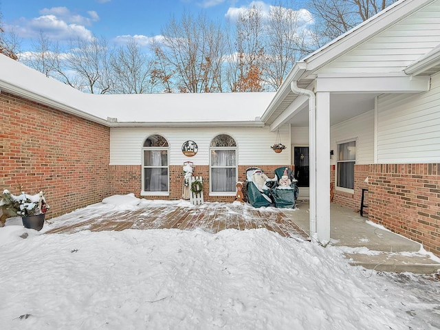 snow covered property entrance featuring a patio and brick siding