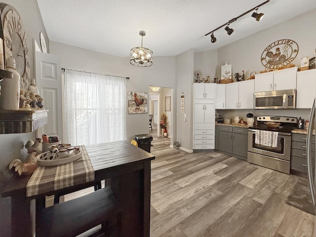 kitchen with a textured ceiling, vaulted ceiling, appliances with stainless steel finishes, light wood finished floors, and an inviting chandelier