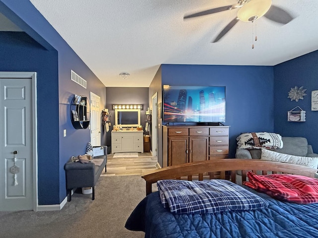 bedroom featuring light colored carpet, visible vents, ensuite bathroom, a textured ceiling, and baseboards