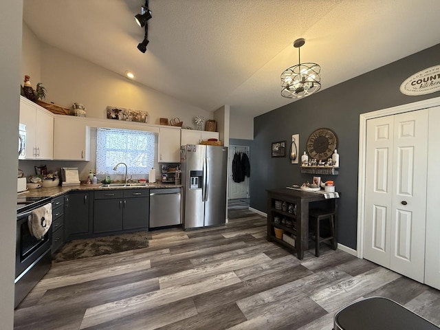 kitchen with dark wood-style floors, stainless steel appliances, white cabinets, vaulted ceiling, and a sink