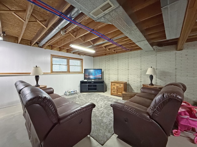 living area featuring concrete flooring, brick wall, and visible vents