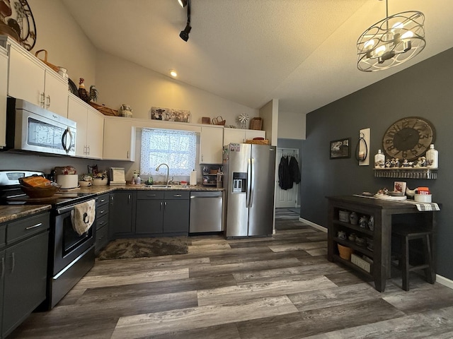 kitchen featuring dark wood-style flooring, appliances with stainless steel finishes, white cabinetry, vaulted ceiling, and a sink