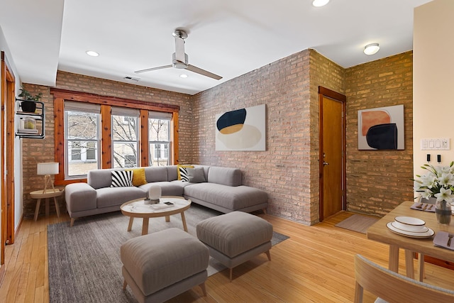 living area featuring a ceiling fan, light wood finished floors, and brick wall