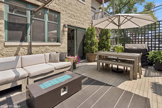 wooden terrace with area for grilling and an outdoor living space with a fire pit