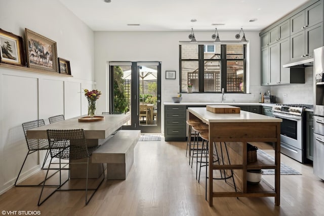 kitchen with sink, gas stove, gray cabinetry, light wood-type flooring, and decorative backsplash