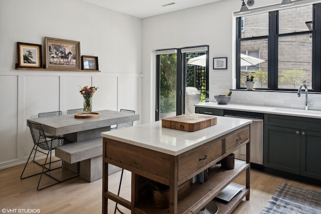 kitchen with sink, stainless steel dishwasher, light hardwood / wood-style floors, and decorative backsplash