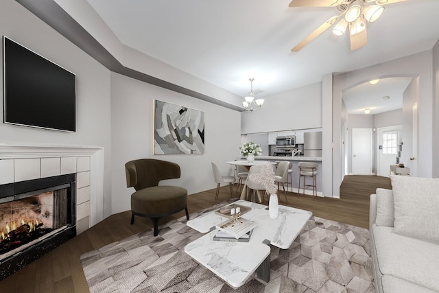 living room featuring a tile fireplace, ceiling fan with notable chandelier, and light wood-type flooring