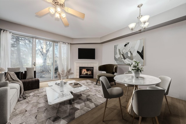 living room with ceiling fan with notable chandelier, light hardwood / wood-style floors, and a tile fireplace