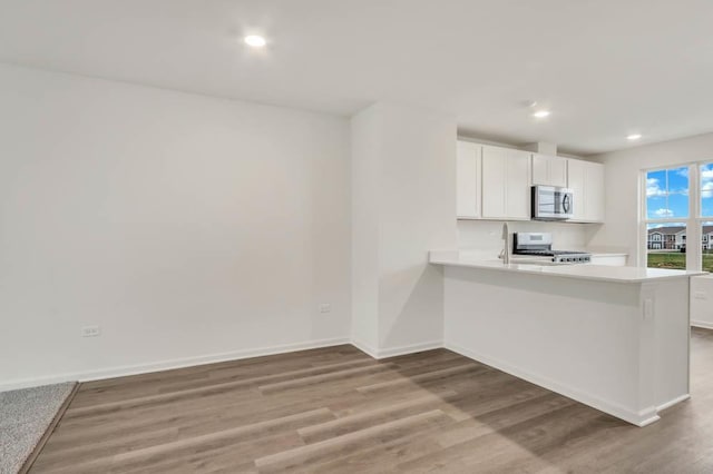 kitchen featuring white cabinets, kitchen peninsula, light hardwood / wood-style flooring, and stove