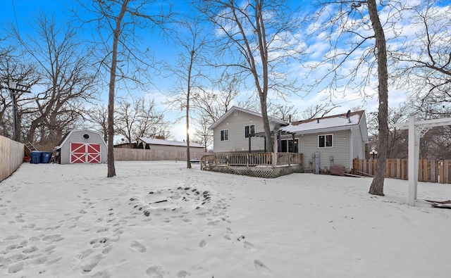 snowy yard featuring a storage shed, a fenced backyard, a detached garage, an outbuilding, and a deck