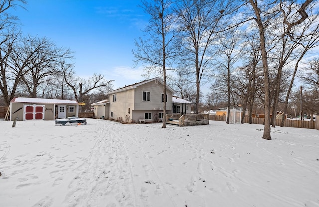 snow covered back of property with a storage shed, fence, and an outdoor structure