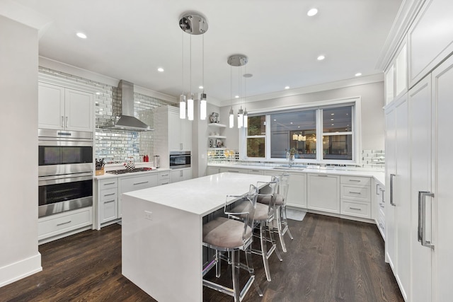 kitchen featuring a kitchen island, wall chimney range hood, white cabinets, and appliances with stainless steel finishes