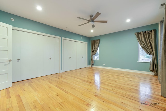 unfurnished bedroom featuring multiple windows, light hardwood / wood-style flooring, and two closets