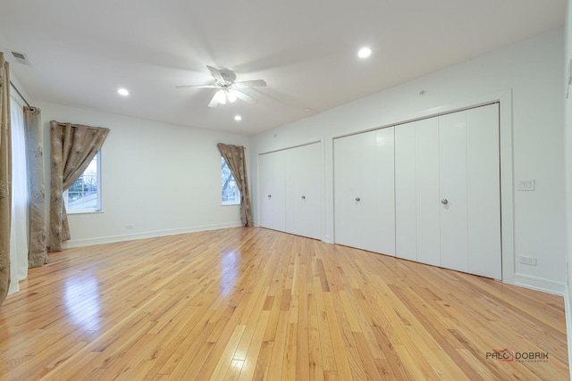 unfurnished bedroom featuring multiple closets, ceiling fan, light wood-type flooring, and multiple windows