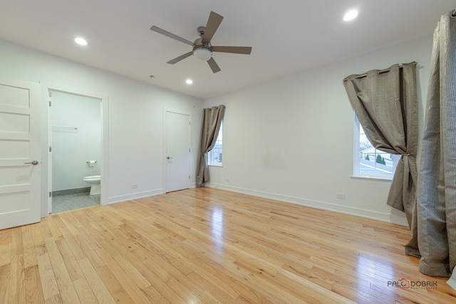 unfurnished bedroom with multiple windows, ensuite bathroom, and light wood-type flooring