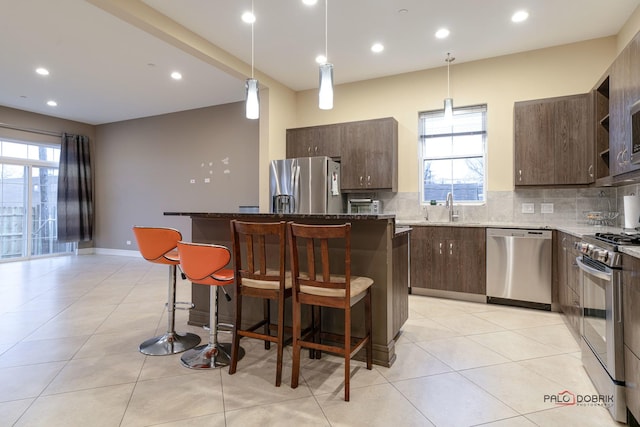 kitchen featuring a breakfast bar area, dark stone countertops, hanging light fixtures, stainless steel appliances, and a center island