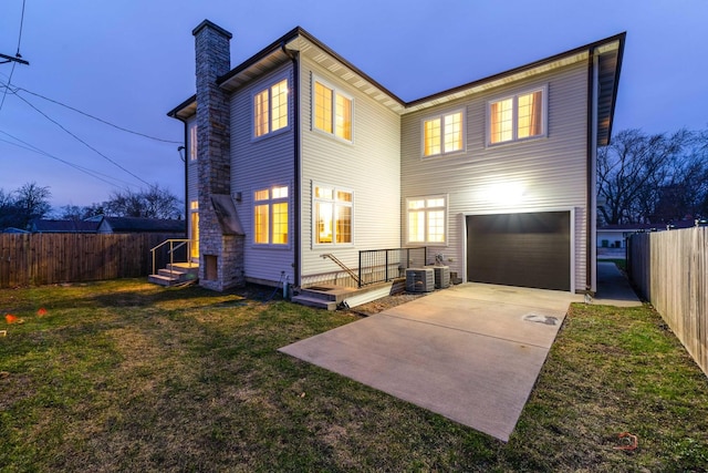 back house at dusk with a garage, central AC, and a lawn