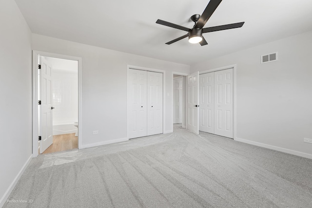 unfurnished bedroom with multiple closets, ensuite bath, ceiling fan, and light carpet